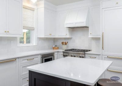 Bright kitchen view with a large white island, stainless steel range, and sleek cabinetry accented by gold hardware.