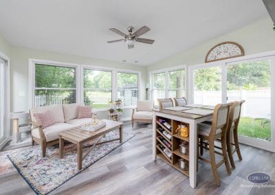 Bright sunroom with sofa, dining island, and ceiling fan overlooking a backyard view.