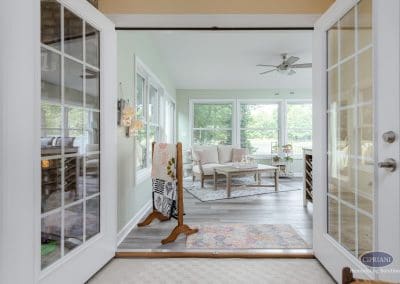 Sunroom view through French doors with loveseat, coffee table, and bright windows.