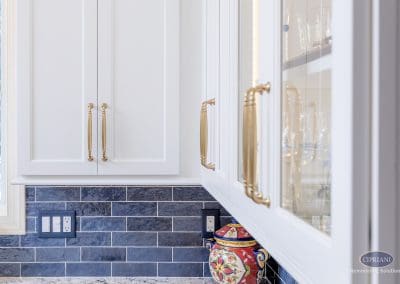 White cabinetry with brass hardware above a navy tile backsplash.
