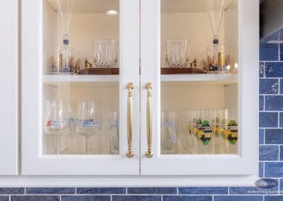 Glass-front kitchen cabinets with brass pulls displaying glassware.