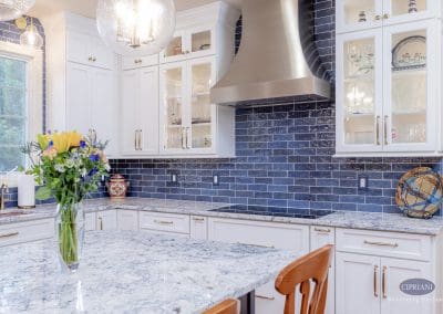 Bright kitchen with navy backsplash and white cabinetry. Stainless steel hood and marble island create a striking focal point.