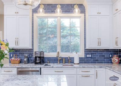 Kitchen sink with large window framed by navy backsplash and white cabinets. Brass faucet adds a touch of elegance.