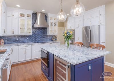 Spacious kitchen with navy island, stainless range hood, and white cabinetry.