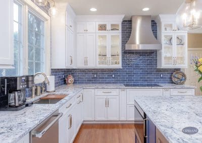 White cabinetry and stainless range hood with navy tile backsplash in remodeled kitchen.