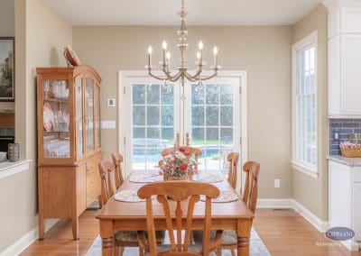 Elegant dining room with wooden table, chandelier, and glass doors opening to backyard pool.