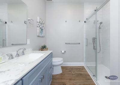 Bathroom with glass shower and gray vanity – A bright bathroom featuring a marble-look vanity, wood-look flooring, and a frameless glass shower.