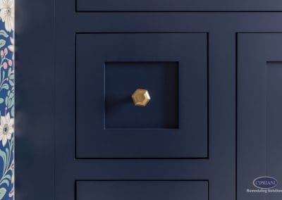 Navy cabinet detail with gold knob – A close-up of a navy vanity drawer with a geometric gold knob and floral wallpaper accent.