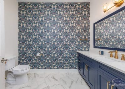 Floral wallpaper with navy vanity – A patterned accent wall with bold floral design complements a navy vanity and gold fixtures in this Collingswood bathroom remodel.