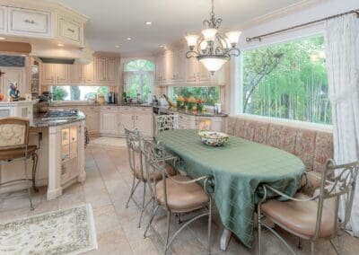 Bright kitchen and breakfast nook with large window. A built-in banquette and soft green tones create a warm, inviting space filled with natural light.