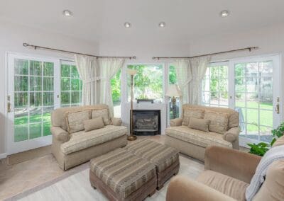 Bright sitting room with fireplace and large windows. Neutral tones and soft light create a calm, inviting retreat with garden views.