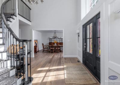 Open foyer sightline An airy interior view showing a curved staircase with iron balusters, wide-plank hardwood floors, and a clear visual connection from the front entry into the dining room.
