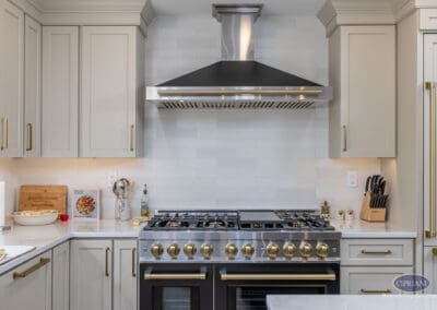 Professional range detail A close-up of a professional-style gas range with brass controls, custom cabinetry, a white tile backsplash, and a statement range hood.