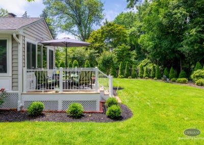 Rear deck addition with seating area, white railing, and landscaped backyard