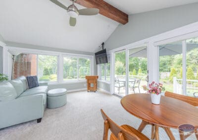 Vaulted sunroom with exposed beam and sliding patio doors A light-filled sunroom featuring a vaulted ceiling with exposed wood beam, ceiling fan, lounge seating, and sliding glass doors that open directly to the rear deck.