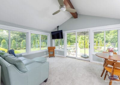 Sunroom with vaulted ceiling, expansive windows, and deck access A bright sunroom featuring a vaulted ceiling with exposed beam, wraparound windows, lounge seating, and sliding doors that open directly to the outdoor deck.