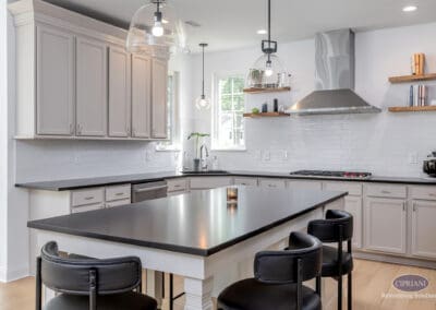 Modern white kitchen with black island, glass pendant lights, stainless steel range hood, and floating wood shelves in a Mount Laurel kitchen remodel.