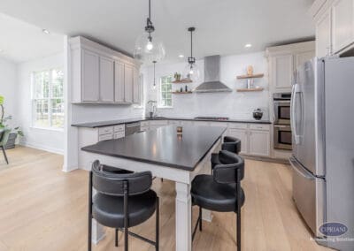 Open Mount Laurel kitchen with a black island, white cabinetry, glass pendant lights, stainless steel appliances, and light wood flooring.