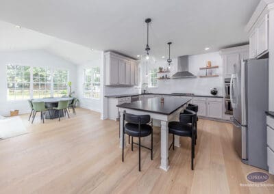 Wide open Mount Laurel kitchen with black island, white cabinetry, glass pendant lights, stainless steel appliances, and adjacent dining area.