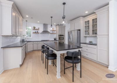 Mount Laurel kitchen with oversized black island, white perimeter cabinetry, glass pendant lighting, stainless steel appliances, and light wood flooring.
