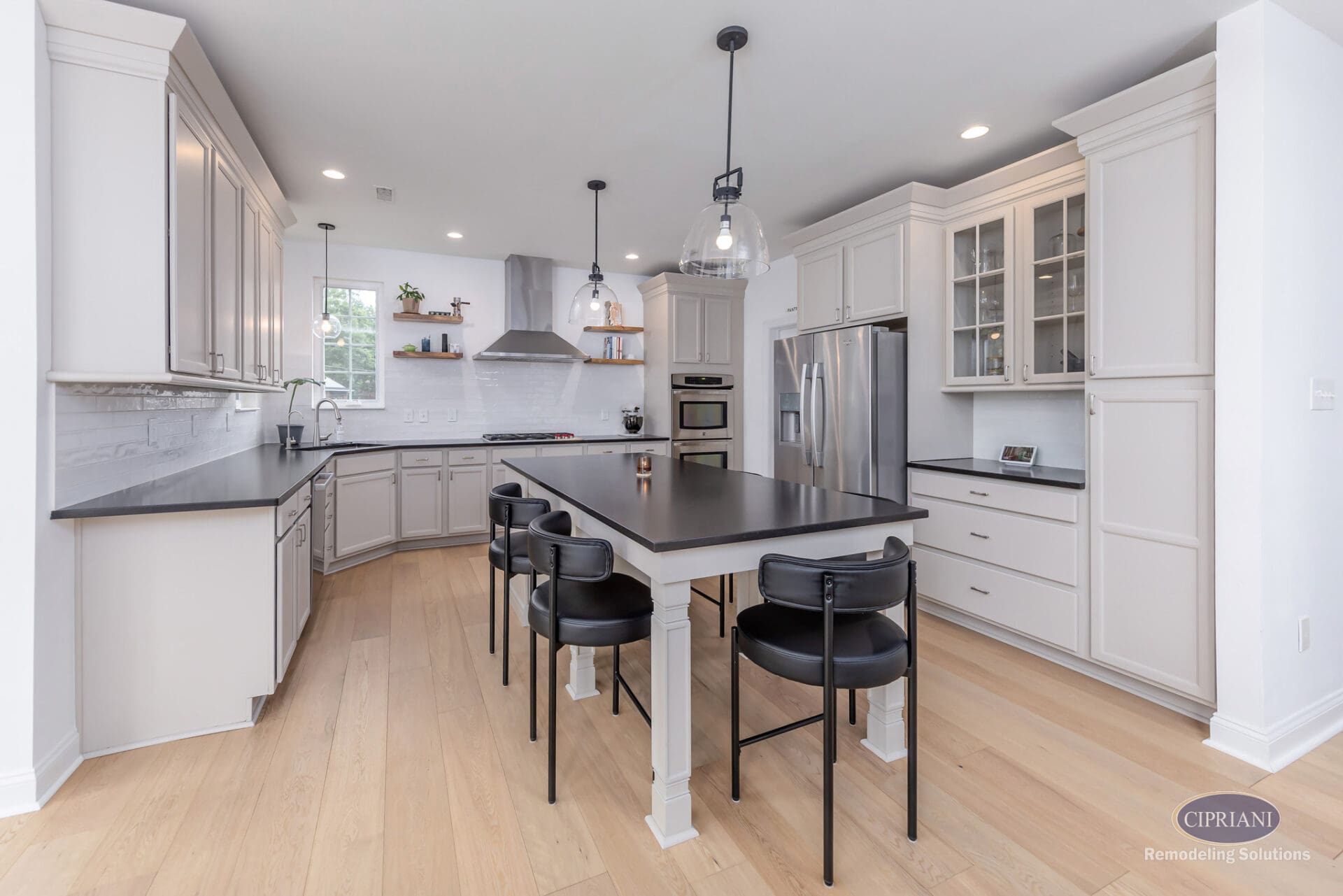 Oversized Island Kitchen Layout | Mount Laurel Kitchen Remodel Mount Laurel kitchen with oversized black island, white perimeter cabinetry, glass pendant lighting, stainless steel appliances, and light wood flooring.