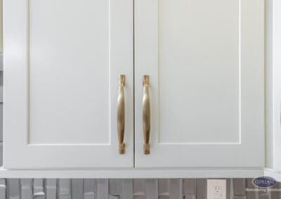 White shaker-style kitchen cabinetry with warm brass hardware, highlighting clean lines and subtle contrast against a textured tile backsplash.