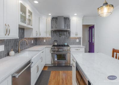 Bright kitchen view highlighting white shaker cabinetry, a professional range with custom hood, marble-look countertops, and a textured gray tile backsplash.