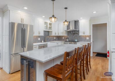 Wide kitchen view featuring a large marble-look island with seating, white shaker cabinetry, stainless steel appliances, and warm brass pendant lighting.