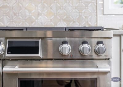 Professional Gas Range Detail with Geometric Tile Backsplash: Close-up of stainless steel gas range controls set against a circular-pattern tile backsplash for a refined, chef-inspired kitchen design.