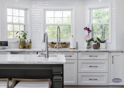 Bright Window-Focused Kitchen Sink Area: Three-window kitchen backdrop highlighting a centered sink, marble countertops, and clean white cabinetry with warm brass accents.