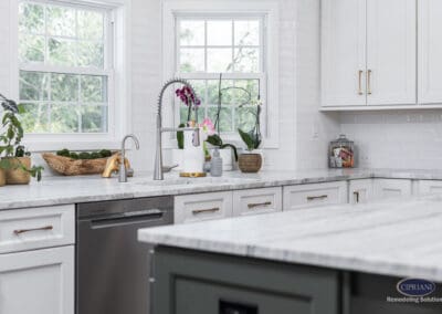 Light-Filled Kitchen Sink Wall with Brass Accents: White cabinetry, marble countertops, and a professional-style faucet centered between double windows with warm brass hardware details.