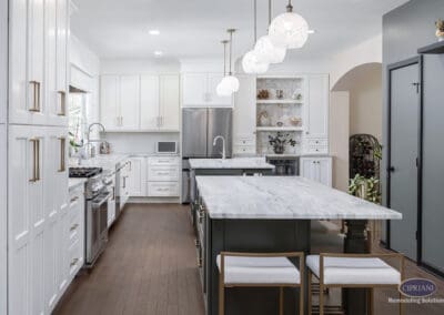 Open Concept Timeless Gathering Kitchen Layout: Mount Laurel kitchen featuring dual marble islands, white shaker cabinetry, custom beverage station, decorative tile niche, and layered pendant lighting in a bright open-concept layout.