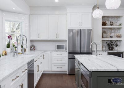 Timeless Gathering Mount Laurel Kitchen Remodel: Custom white kitchen with marble countertops, dual workstations, stainless steel refrigerator, and decorative open shelving designed for elegant everyday functionality.