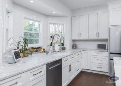 Timeless Gathering Mount Laurel Kitchen Remodel: Bright window-lined kitchen with marble countertops, white shaker cabinetry, gold hardware accents, and farmhouse sink designed for functional daily use.