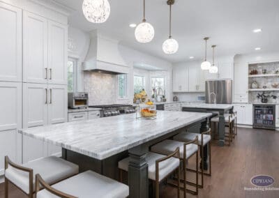 Timeless Gathering Mount Laurel Kitchen Remodel: Large marble island with seating, custom white cabinetry, statement range hood, and layered pendant lighting creating a bright luxury kitchen.