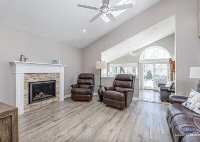 Open concept living room with vaulted ceiling, fireplace feature wall, warm wood-look flooring, and comfortable seating connecting to adjacent sunroom space.