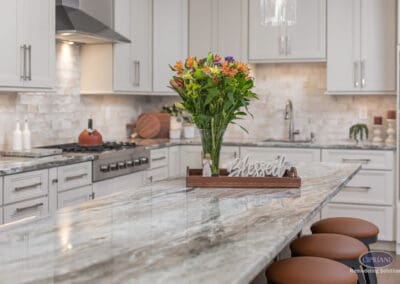 Stone kitchen island with natural veining and decorative centerpiece. Soft neutral cabinetry and layered textures create a calm, inviting focal point.