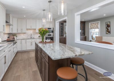 Warm transitional kitchen with two-tone cabinetry and large natural stone island. Glass pendant lighting and open sightlines create a bright, connected entertaining space.