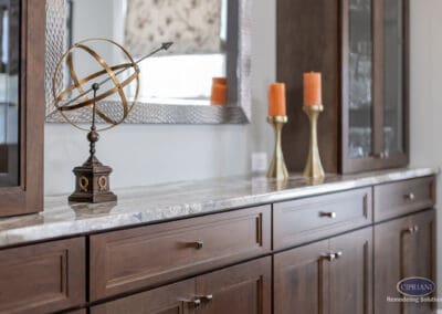 Warm wood buffet cabinetry with stone countertop, geometric hardware, and decorative styling with candles and sculptural accessories.