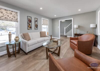 Open-concept sitting area with warm leather chairs and neutral sofa. Soft finishes and layered textures create a comfortable lounge space connected to the kitchen.