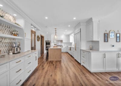 Wide view of kitchen with large island, white cabinetry, open shelving, and warm wood flooring