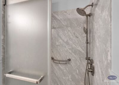 Walk-in shower with glass door, stone-look wall panels, and dual shower head system