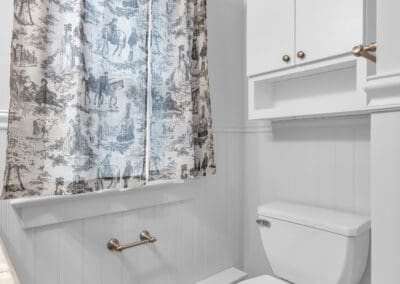 Bathroom with toilet, beadboard walls, wall cabinet, and patterned shower curtain