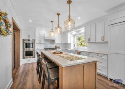 Large kitchen island with seating, glass pendant lights, and white cabinetry with brass hardware