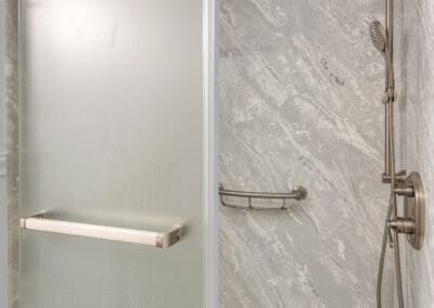 Walk-in shower with frosted glass sliding door, stone-look wall panels, and dual shower head system