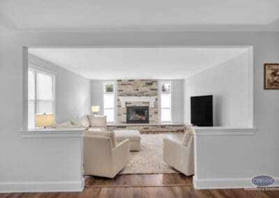 Living room with stone fireplace, neutral seating, and open view from kitchen