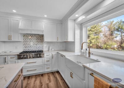 Kitchen corner with farmhouse sink, gas range, white cabinetry, and patterned backsplash