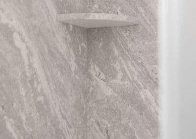 Corner shower shelves in stone-look material integrated into shower wall