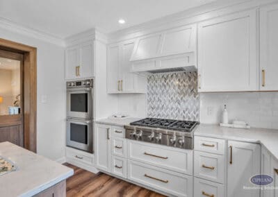 Kitchen with gas range, custom hood, double wall ovens, and patterned tile backsplash