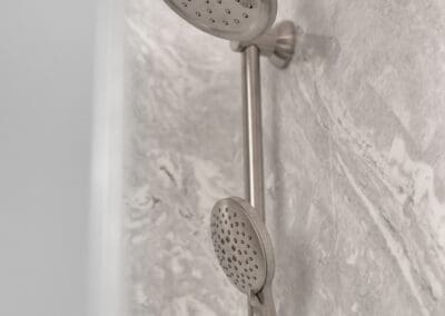 Rain shower head and handheld sprayer mounted on sliding bar against stone-look wall
